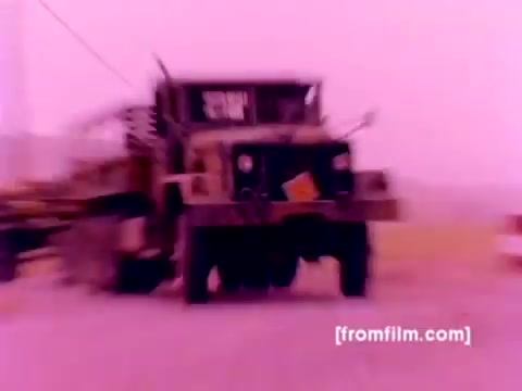 The still from the 'USMC Aviation Ordnance enlistment film' features military vehicles and aircraft, showcasing the Ordnance Option for enlistment.   - **Aircraft Involved**: Includes the F-4 Phantom, AH-1 Super Cobra, FA-18, and Harrier, emphasizing the diverse capabilities of Marine aviation. - **Ordnance Operations**: Highlights the process of mounting missiles and bombs, crucial for air support missions. - **Overall Tone**: The image is affected by a pink tint typical of 16mm negatives, which could be corrected for enhanced clarity and accurate color representation.   The scene encapsulates the rigorous operational environment and technological prowess of the Marine Corps Aviation division.