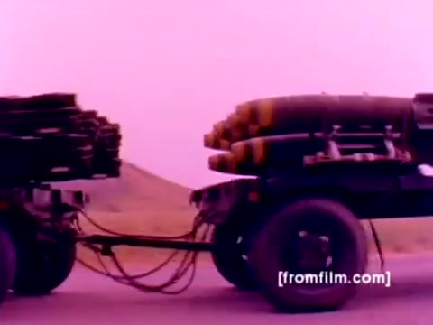 The still from the 'USMC Aviation Ordnance enlistment film' features a military vehicle transporting ordnance, including missiles and bombs, showing the logistical aspects of the Marine Corps' aviation arm. The image has a retro aesthetic typical of 16mm footage, with colors slightly muted. Better color correction would reveal more detail in the ordnance and the surrounding landscape, enhancing the overall clarity and vibrancy of the scene. The focus on military equipment underscores the film's emphasis on the ordnance specialist role in the Marine Corps.