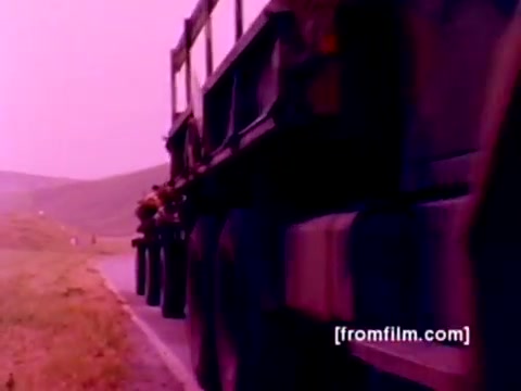 The still from the 'USMC Aviation Ordnance enlistment film' features a transport truck on a road, with focus on its wheels and chassis. The image showcases a pinkish hue indicative of the 16mm film’s age and color correction issues. Surrounding scenery includes grassy hills, suggesting a military training or operational environment. The film emphasizes military readiness, particularly in relation to ordnance handling and aerial support aircraft, including F-4 Phantoms, AH-1 SuperCobras, FA-18 Hornets, and Harriers. Despite being silent, the visuals effectively convey the dynamics of aviation ordnance operations.
