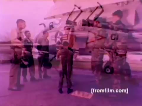 The still from the 'USMC Aviation Ordnance enlistment film' captures a moment with several Marines gathered around an aircraft—likely an F-4 Phantom or a similar model. The image features a mix of personnel in military attire, including a child, possibly a family member or a recruit, engaging with the group.   Ordnance, such as missiles and bombs, is being prepared for mounting, emphasizing the technical and operational aspects of aviation ordnance. The color correction would enhance details, providing a clearer and more vibrant representation of the scene against the backdrop of military aviation, showcasing the importance of ordnance in Marine Corps operations.