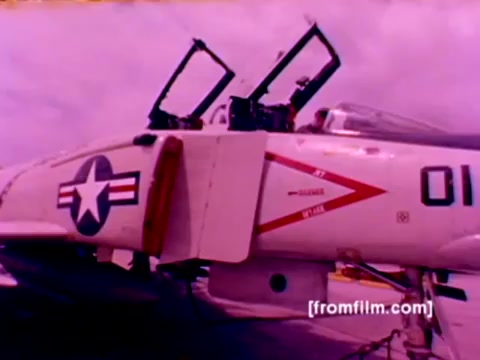 The still from the 'USMC Aviation Ordnance enlistment film' captures a moment showcasing military aviation. Key elements include:  - **Aircraft Featured**: F-4 Phantoms, AH-1 SuperCobras, an FA-18 Hornet, and a Harrier. - **Ordnance Activity**: The image depicts the mounting of missiles and bombs, emphasizing the ordnance aspect of the enlistment option. - **Visual Characteristics**: The 16mm negative shows a slightly faded color palette, with an emphasis on various aircraft features.  The still presents a glimpse into Marine Corps aviation and the critical role of ordnance in military operations, all within the context of recruiting for the Ordnance Option.