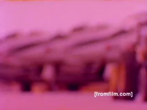 The still from the 'USMC Aviation Ordnance enlistment film' features various Marine Corps aircraft, including F-4 Phantoms, AH-1 SuperCobras, an FA-18, and a Harrier. The scene showcases ordnance being mounted, with missiles and bombs visible. The color rendering from the 16mm negative is soft, likely due to age, but the military aircraft's silhouettes are distinguishable, emphasizing the technical aspects of aviation ordnance in a military context. The overall mood is one of dedication and precision, characteristic of military enlistment films.