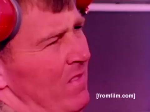 This still from the 'USMC Aviation Ordnance enlistment film' captures a close-up of a Marine, likely involved in ordnance handling. His expression appears focused or intense, reflecting the seriousness of the task at hand. The background suggests a military environment, perhaps near aircraft like the F-4 Phantom or AH-1 SuperCobra, which feature prominently in the film. The color appears somewhat muted due to the 16mm negative, with potential for improved correction to enhance details and clarity.  The context of the film emphasizes the 'Ordnance Option' for enlistment, showcasing the crucial role of aviation ordnance in the Marine Corps, with visuals of missiles and bombs being mounted on aircraft.