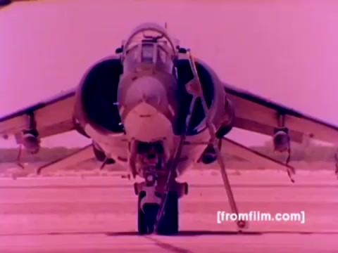 The still from the 'USMC Aviation Ordnance enlistment film' features a close-up of a Harrier jet, showcasing its distinctive nose and cockpit design. The aircraft is positioned prominently on the runway, highlighting its readiness for operations. The scene likely conveys the advanced technology and capabilities of Marine Corps aviation, emphasizing the ordnance aspect with visual elements related to weaponry. Overall, the still captures the essence of military aviation and enlistment in the ordnance field.