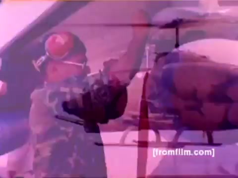 The 16mm still from the 'USMC Aviation Ordnance enlistment film' showcases a Marine in uniform, working diligently to mount ordnance on an aircraft, likely an AH-1 SuperCobra. The scene highlights important military equipment, including F-4 Phantoms, an FA-18, and a Harrier, emphasizing the ordnance option available for enlistment. The background suggests a busy airfield environment, underscoring the dynamic nature of aviation ordnance work. The color in the still can be better corrected to enhance the clarity and vibrancy of the military setting and equipment.