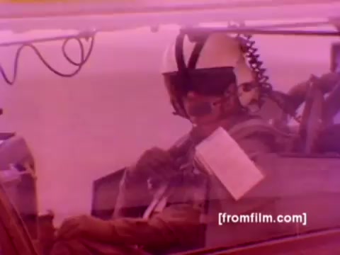 The still from the 'USMC Aviation Ordnance enlistment film' features military aircraft, including F-4 Phantoms, AH-1 SuperCobras, an FA-18, and a Harrier. It showcases the process of ordnance being mounted, including the attachment of missiles and bombs. The image is derived from a 16mm negative, with an emphasis on improved color correction, revealing the operational environment and aircraft details vividly. The scene suggests action and technical proficiency associated with Marine Corps aviation.
