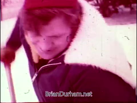 The still from 'Campbell's Soup - The Manhandlers' features a man in a winter scene, dressed in a warm jacket and a red hat, engaged in an activity that suggests effort or work, possibly shoveling snow. The ambiance reflects a playful, outdoor theme, aligning with the upbeat tone of Frankie Laine's theme song. The visual style indicates a vintage film aesthetic typical of the 16mm format.