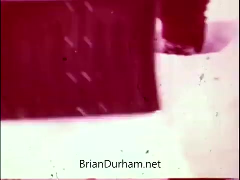 The 16mm still from 'Campbell's Soup - The Manhandlers' features a distinctive color palette with a reddish tint, emphasizing a nostalgic and playful aesthetic. The scene likely involves a humorous or whimsical portrayal related to the themes of the advertising campaign, underlined by Frankie Laine's theme song. The overall composition may capture the essence of the mid-20th century advertising style.