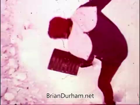 The still from 'Campbell's Soup - The Manhandlers' features a figure shoveling in a snowy environment. The color palette appears warm, primarily shades of pink and red, creating a nostalgic feel. The scene aligns with the upbeat theme song by Frankie Laine, highlighting a whimsical, lighthearted approach to everyday activities.