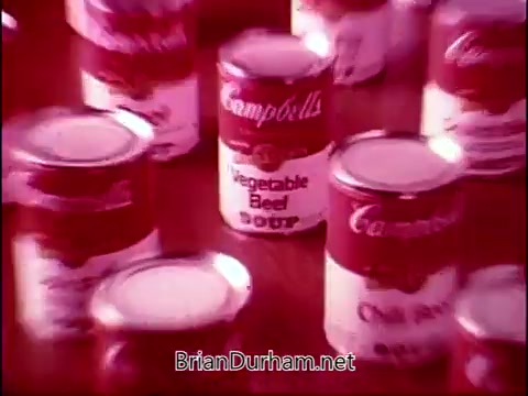 The still from 'Campbell's Soup - The Manhandlers' features a vibrant arrangement of Campbell's Soup cans, prominently showcasing the 'Vegetable Beef Soup' label among others. The overall aesthetic is nostalgic, reflecting the mid-20th century style of advertising, with a warm color palette that emphasizes the iconic branding. The theme song by Frankie Laine adds a catchy, melodic element to the commercial, enhancing its appeal.
