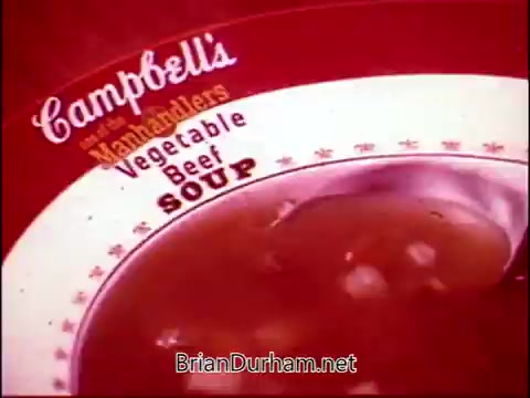 The still from 'Campbell's Soup - The Manhandlers' features a close-up of a bowl of thick, hearty soup, specifically highlighting Vegetable Beef Soup. The vibrant red background emphasizes the Campbell's Soup brand, with classic lettering and design elements framing the bowl. The context suggests a playful or engaging atmosphere, likely enhanced by Frankie Laine's theme song.