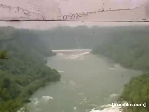 The still captures a serene view of a river winding through lush greenery, likely depicting the landscape around Niagara Falls or similar natural settings in the Rochester area during the late 1940s. The image has a vintage quality characteristic of 16mm film, with visible scratches, contributing to its nostalgic feel. It reflects a peaceful moment in nature, possibly representing leisure or exploration during that time period.
