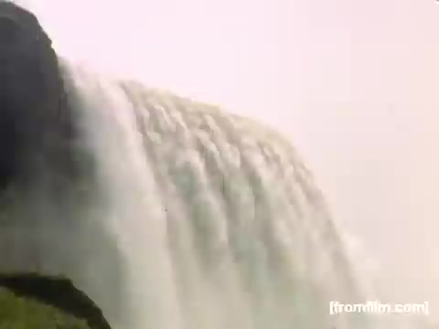 The still captures a close-up view of a cascading waterfall, likely from Niagara Falls, showcasing the powerful rush of water as it flows over the edge. The image highlights the natural beauty and force of the falls, characteristic of the region during the late 1940s. The surrounding landscape appears lush, indicating a vibrant, natural setting typical of the era's home movies.