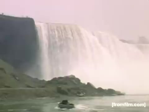 The still captures a view of Niagara Falls, showcasing the powerful cascade of water. A small boat is visible in the foreground, emphasizing the scale of the falls. The scene is bathed in a soft, hazy light, reflecting the mood of the late 1940s. This image is part of a documentary exploring everyday life and notable sites in Rochester and Niagara Falls during that time period.