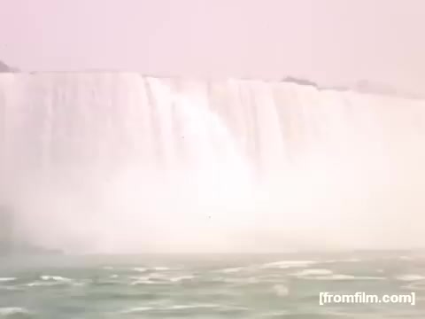 The still captures a view of Niagara Falls, showcasing the powerful cascade of water plunging over the edge. The image has a soft, nostalgic quality characteristic of 16mm film from the late 1940s, emphasizing the mist and the serene yet majestic atmosphere of the natural landmark. The color palette reflects a vintage look, enhancing the sense of time and place from the period of 1948-1950.