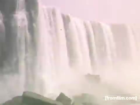 The still depicts a serene view of Niagara Falls, showcasing the powerful cascades of water flowing over the edge. The scene is softened by a mist that rises from the falls, enhancing the natural beauty of the landscape. This image captures the essence of the 1948-1950 period, highlighting the iconic attraction's grandeur and appeal. The use of 16mm film adds a nostalgic quality, evoking a sense of history and wonder.