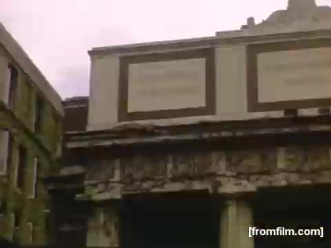 The still from 'Home Movies: Rochester/Niagara Falls 1948-1950' depicts a dated building façade showing signs of decay, with peeling paint and boarded-up windows. The architectural details suggest it was once a prominent structure, possibly a theater or a public space, now in a state of disrepair. The overall atmosphere conveys a sense of nostalgia for a past era, reflecting the changes in the urban landscape during that time period.