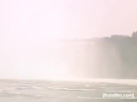 The still depicts a misty scene near a waterfall, likely Niagara Falls, featuring soft colors and a hazy atmosphere. The focus is on the cascading water and surrounding landscape, conveying a serene yet powerful natural setting from the late 1940s.