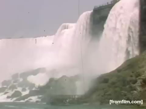 The still captures a moment from the 16mm film 'Home Movies: Rochester/Niagara Falls 1948-1950,' showcasing the majestic flow of water cascading over Niagara Falls. The image focuses on the powerful falls, with mist rising and surrounding the rocky landscape, conveying the natural beauty of the iconic location during the late 1940s.