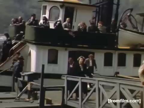 The still is from 'Home Movies: Rochester/Niagara Falls 1948-1950,' depicting a crowded boat at dock with passengers visible on both the deck and the walkway. People are engaged in various activities, some waving, creating a lively atmosphere. The scene captures a moment of leisure and travel during that era. The colors suggest a vibrant depiction, typical of home movie footage from the late 1940s to early 1950s.