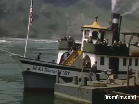 The still features the 'Maid of the Mist,' a historic boat known for ferrying tourists close to Niagara Falls. The vessel is docked, showcasing a vibrant design with a yellow and black color scheme, and is adorned with an American flag. Passengers can be seen on board, likely preparing for a scenic tour. The backdrop features the natural beauty of the Niagara region, emphasizing its appeal as a tourist destination in the late 1940s.