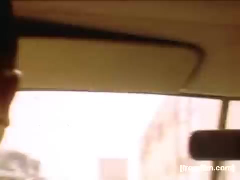 The still captures a moment inside a vehicle, likely from the 1940s to 1950s based on its context. The perspective shows a view of the dashboard and part of the driver or passenger's head, with a bright, possibly sunlit outside scene visible. The ambiance suggests a casual or familial setting, highlighting everyday life during that era, fitting the theme of home movies documenting personal experiences in Rochester and Niagara Falls.