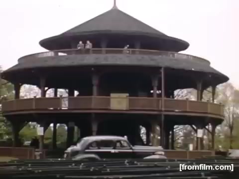The still features a multi-tiered wooden gazebo, likely located in a park, surrounded by greenery. A vintage car is seen passing by, hinting at the mid-20th century setting. The image captures a leisurely scene, embodying the outdoor recreational culture of the late 1940s in the Rochester/Niagara Falls area.