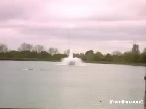 The still depicts a scene from 'Home Movies: Rochester/Niagara Falls 1948-1950,' showcasing a water splash, likely from a boat or aquatic activity, set against a cloudy sky. The image captures a moment of action over a tranquil body of water, with trees lining the shore, emphasizing a serene yet dynamic atmosphere characteristic of home movies from that era.