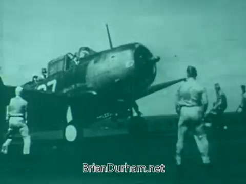 The still depicts a military aircraft on a runway, surrounded by servicemen in uniform. The image has a greenish tint typical of 1960s film, emphasizing the aviation theme while focusing on the interaction between the personnel and the plane, likely aimed at commemorating Veterans Day.