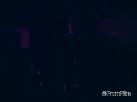 The still from the film about NTID Rochester Institute of Technology depicts a dimly lit scene, suggesting a focus on a person or group engaged in a task. The context emphasizes the capabilities of deaf individuals and the importance of training, underscoring the message that with the right education, deaf people can excel in various fields. The visual atmosphere possibly reflects an environment of learning and skill development.