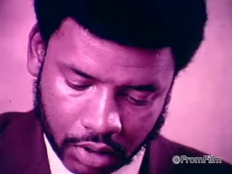 The still features a man with a thoughtful expression, engaged in a task or study, possibly reading or writing. His hairstyle is styled, and he has a beard. The background has a soft focus, hinting at a classroom or similar educational setting. This image likely reflects the theme of empowerment and the potential for deaf individuals to gain skills and training, aligning with the voiceover's message about the capabilities of deaf people.