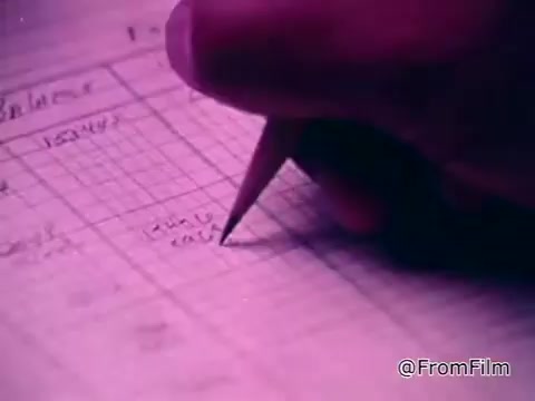 The still depicts a close-up of a hand holding a pencil, writing on a sheet of graph paper. The background is tinged with purple hues, possibly indicating an artistic filter or lighting. The context emphasizes the capabilities of deaf individuals, highlighting the importance of training and education, such as that provided by the NTID at Rochester Institute of Technology. The focus is on the act of writing, symbolizing learning and skill development.