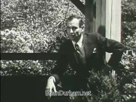 The still from the 1968 PSA for the Junior GI Bill features a man in a formal suit leaning against a railing, suggesting a casual yet serious demeanor. The background shows greenery, indicating an outdoor setting. The overall tone of the image hints at encouraging the audience to consider the benefits of the Junior GI Bill.