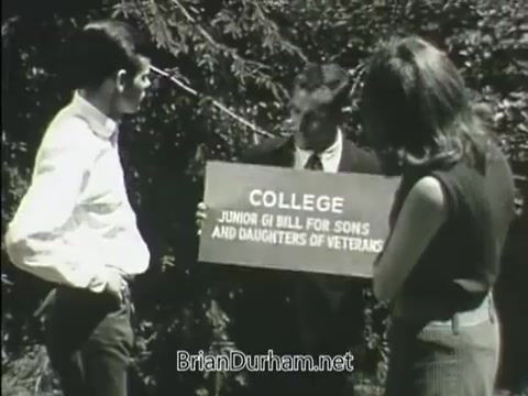 The still from the 1968 'Junior GI Bill PSA' depicts a man in a suit holding a sign that reads 'COLLEGE JUNIOR GI BILL FOR SONS AND DAUGHTERS OF VETERANS.' He is flanked by two young individuals—one male and one female—who appear to be attentively listening. The background features greenery, suggesting an outdoor setting. The scene promotes educational opportunities for children of veterans.