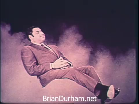 The still from the 1968 Niagara Rolla-ssage chair commercial conveys a sense of relaxation amidst a hectic environment. A man in a suit appears to be floating or reclining comfortably, embodying the message of comfort and tranquility. The commercial emphasizes the importance of self-care for those engaged in significant work, suggesting that investing in a Niagara Rolla-ssage chair leads to a more enjoyable and restful experience. The overall tone is one of urgency turned into relief, showcasing the juxtaposition of a busy lifestyle with the need for personal comfort.
