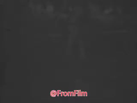 In this still from the 1969 Aetna Automobile Safety PSA titled 'Inattention,' two women are engaged in a light conversation, likely while waiting for a ride or walking together. The dialogue reflects casual topics such as fashion, hinting at an upcoming event. Woman 1 expresses eagerness to see new styles, and Woman 2 compliments her, suggesting a friendly dynamic. The overall tone is upbeat, contrasting with the serious theme of road safety that the PSA aims to address, emphasizing the dangers of inattention while driving.