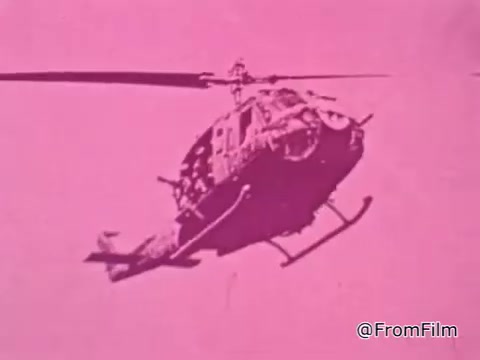 The still from the 1968 PSA 'Mail Early to Your Soldier' features a helicopter, likely a representation of military transportation during the Vietnam War. The image is predominantly in a striking pink hue, which may have been used for visual impact or stylistic choice typical of the era's film techniques. The context of the PSA emphasizes the importance of timely communication and the shipping of gifts to servicemen overseas, suggesting a sense of urgency and care from loved ones back home. The helicopter symbolizes the connection between the home front and the servicemen in active duty, highlighting the military setting of the message.