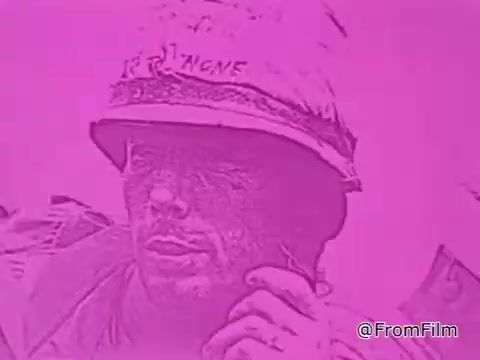 The still from the 1968 PSA 'Mail Early to Your Soldier' is presented in a striking pink hue, which adds a unique visual element to the scene. It likely features a soldier in a combat helmet, showing a contemplative expression. The soldier's face appears weathered, hinting at the realities of serving in a war zone, possibly reflecting the emotional weight of being away from home during the holidays. The PSA's context emphasizes the importance of timely communication and sending care packages to servicemen overseas, reinforcing feelings of connection and support from loved ones back home. The overall tone is both urgent and heartfelt, conveying a message of care and remembrance during the holiday season.