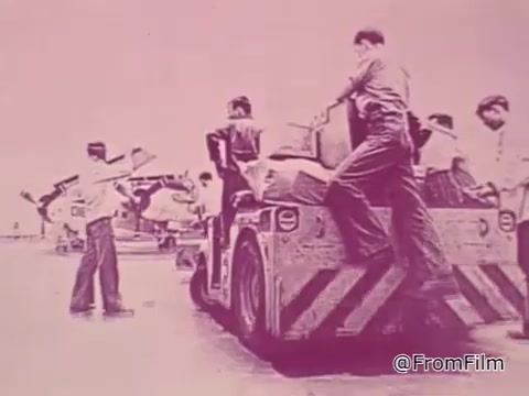 The still from the 1968 PSA 'Mail Early to Your Soldier' features a scene at a military airport, highlighting the logistics of sending packages to servicemen stationed overseas.   In the image, several individuals are engaged in handling packages, suggesting a sense of urgency and teamwork. One person is seen operating a vehicle designed for transporting cargo, while others appear to be loading boxes onto it. The atmosphere conveys a busy operational environment typical of military logistics.  The overall color tone is likely muted, with a pinkish hue, reflective of the period's film quality. This visual context complements the voice-over's message about ensuring mail arrives on time, emphasizing the importance of timely communication and support for soldiers during the holiday season. The deadline mentioned adds a layer of