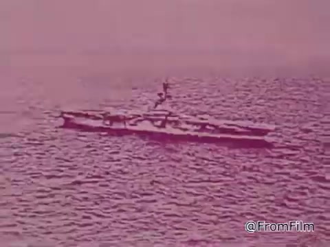 The still from the 1968 PSA 'Mail Early to Your Soldier' depicts a military ship on the water. The image has a pinkish hue, likely due to the color grading of the time or aesthetic choice, creating a nostalgic and somber atmosphere. Sailors can be seen on the deck, possibly engaged in activities related to the ship's operations.   The context focuses on the importance of timely mailing for holiday gifts to servicemen stationed overseas, emphasizing careful preparation and clear addressing. This visual reinforces the message of connection and support for military personnel during the Vietnam War era. The overall tone is one of encouragement and community involvement, urging viewers to participate in ensuring their loved ones receive their gifts on time for the holidays.