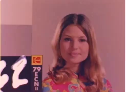 The still features a young woman with long, wavy hair, wearing a brightly colored, patterned top. The background is softly lit, helping to emphasize her light complexion. In the foreground, there is a film label indicating '79 ECN II,' typical for a 16mm negative. The overall aesthetic reflects a vintage style from the early 1980s.