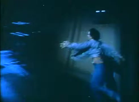 In the still from the 'Love Child' trailer, a person is seen running in a dimly lit environment. The scene is characterized by a blue hue, creating a tense atmosphere. The figure appears desperate, with their arms outstretched, suggesting urgency or fear. The low lighting and shadows contribute to a sense of intrigue and drama within the narrative.
