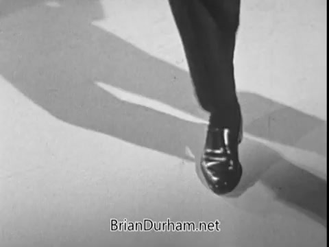 The still from the late 1960s Heart Fund PSA featuring Ray Bolger shows a close-up of a polished black shoe walking on a light surface. The focus on the footwear highlights the action of movement, likely symbolizing health and activity related to the campaign's message. The overall tone is professional and purposeful, fitting the context of a public service announcement.