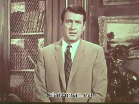 The still features a man in a light-colored suit and a tie, standing in an interior setting that includes bookshelves and decorative elements. He appears to be delivering a message, likely relating to health awareness, specifically about multiple sclerosis. The context suggests a public service announcement aimed at educating viewers on the condition.