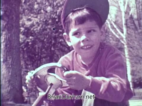 The still features a young boy wearing a cap, engaged with a toy steering wheel while outdoors. His expression conveys concentration and curiosity. The scene likely reflects the importance of vision in childhood activities, aligning with the PSA's message about amblyopia and the need for early detection of eye problems. The background hints at a natural setting, reinforcing the theme of active childhood.