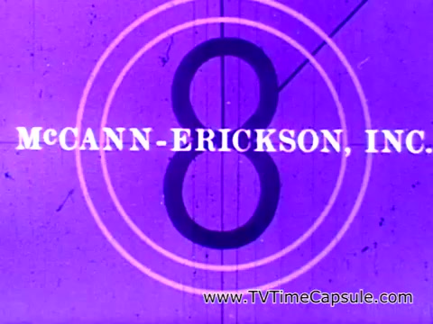 The 16mm still features a purple background with a prominent circular countdown, displaying the number '8.' Above the circle, the text 'McCANN-ERICKSON, INC.' is visible, indicating the advertising agency responsible for the campaign. This still is likely from the production aspect of the iconic Coca-Cola commercial 'I'd like to teach the world to sing,' which promotes themes of unity and joy.