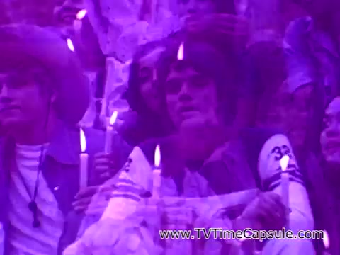 The still from 'Coca-Cola - I'd Like to Teach the World to Sing' captures a group of diverse individuals holding candles, conveying a sense of unity and togetherness. The soft purple hue adds a dreamy atmosphere, emphasizing the themes of peace and harmony in the context of the iconic advertisement.
