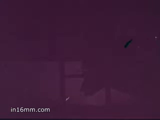 The still depicts a 1968 Vietnam-era Air Force ROTC recruiting commercial featuring an F-4 Phantom II. The image has a reddish tint, possibly due to film degradation or color balancing issues over time. The aircraft appears in a shadowy form, highlighting its silhouette against a blurred background, which may suggest movement or action. This still captures the essence of the era’s military recruitment efforts during the Vietnam War period.