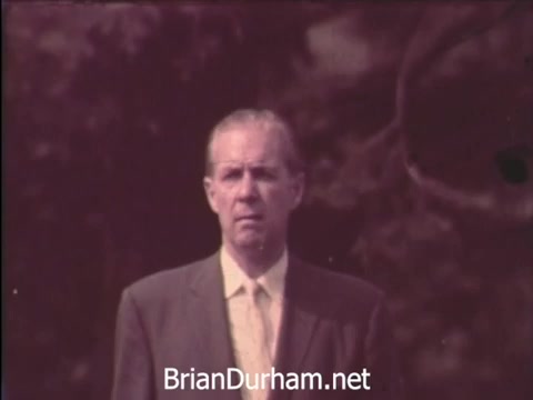 The still from 'A Matter of Life and Breath PSA - Emphysema' depicts a middle-aged man in a suit, standing outdoors. He has a serious expression, reflecting the weight of his condition. The background is blurred, suggesting a focus on his concern about breathing difficulties and the realization of his emphysema diagnosis. The overall tone conveys a sense of urgency and the importance of awareness regarding respiratory health.