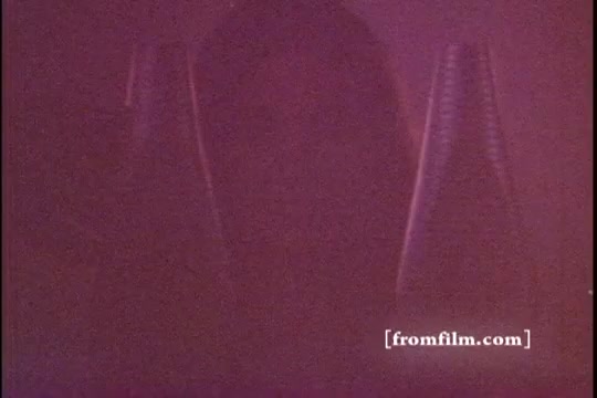 The still from the 'Twice as Nice' shampoo commercial features a blurred, shadowy silhouette of a figure in the foreground, flanked by two shampoo bottles. The image has a soft focus and a warm, reddish-purple tint characteristic of 1970s film. The overall aesthetic conveys a nostalgic, intimate atmosphere typical of vintage advertisements.